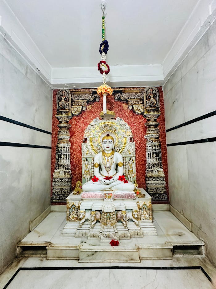 Marble statue of a Jain deity in an ornately decorated temple alcove, serene and peaceful.